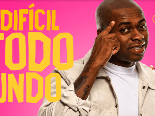 Imagem promocional com fundo rosa vibrante onde se destaca, à esquerda, o texto "TÁ DIFÍCIL PRA TODO MUNDO" escrito em letras amarelas e brancas. No centro, um homem negro sorri apontando o dedo indicador para a própria cabeça. Ele está cercado por dois pequenos cupidos negros de asas brancas e fralda segurando arco e flecha, além de um desenho de coração partido na parte superior.
