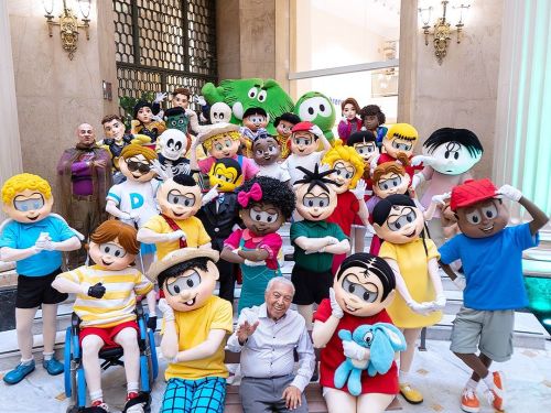 Foto do desenhista Mauricio de Souza sentado com todos os personagens da turma da monica ao seu redor 