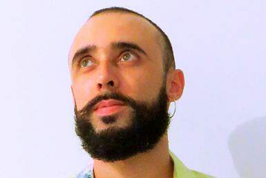 Homem de pele clara, cabelos escuros e curtos, de barba e bigode, olhando lateralmente para cima.
