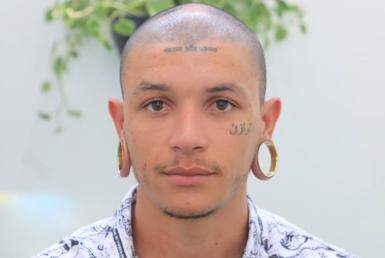 Homem jovem, de cabeça raspada, com tatuagens no rosto, usando alargador nas orelhas.