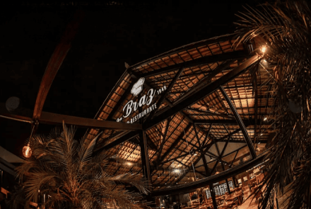 Imagem de uma bar, todo de madeira e palmeiras em volta.