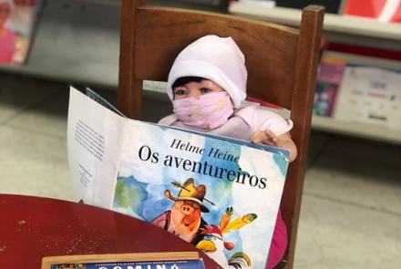 Boneca de mascara segurando um livro infantil