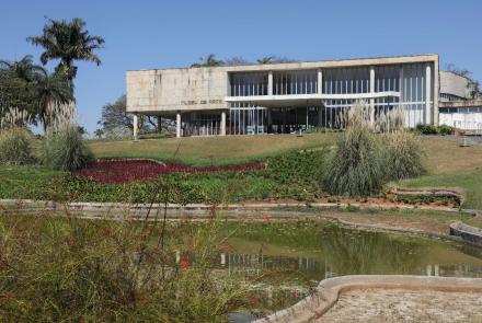 A imagem mostra a fachada do Museu de Arte da Pampulha. É possível observar os jardins do espaço, com o lago, gramado, e ávores