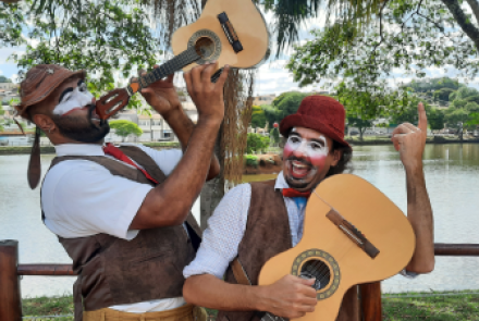 A dupla Zé Viola e Cavaquinho caracterizados com pintura e roupas de palhaço, segurando uma viola e um cavaquinho.