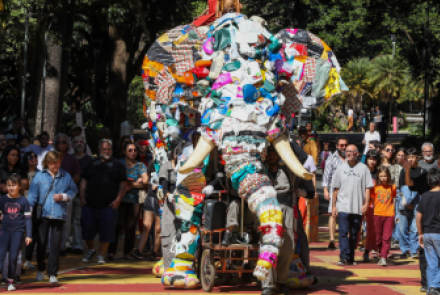 Um Elefante gigante feito de materiais recicláveis e manipulado por atores anda pelas ruas da cidade
