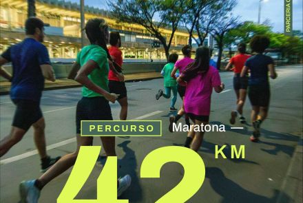 Foto de corredores em movimento, no asfalto, durante a noite. Em destaque sobre a imagem, o texto em amarelo neon: “Percurso – Maratona 42km”