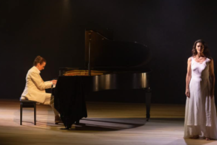 Imagem de um homem tocando piano e uma mulher em pé ao lado com o vestido branco