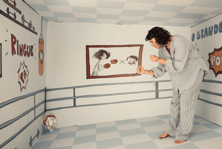 Imagem de uma mulher em um quarto desenhado, com um desenho de uma criança, simulando uma "luta"