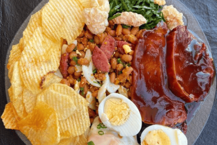 Esta é uma imagem de um prato de comida farta e colorida, típico da culinária brasileira (estilo Feijão Tropeiro ou Virado), servido em um prato escuro sobre uma superfície preta.