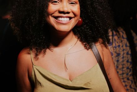 Uma mulher preta cis de cabelo cacheado volumoso com um vestido verde musgo