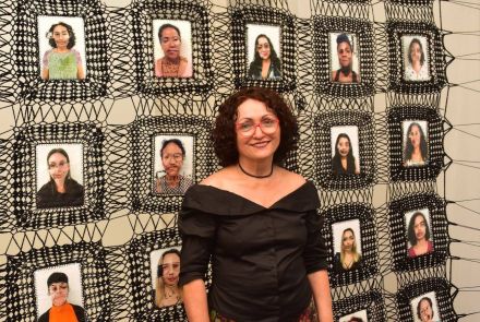 Foto da artista Marlene Barros na frente de uma de suas obras 