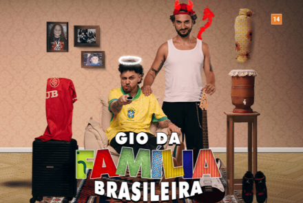 Cartaz do espetáculo "Gio da Família Brasileira" (classificação 14 anos). Em um cenário doméstico, dois homens estão ao centro: um sentado com a camisa da seleção e auréola de anjo, e outro em pé atrás dele com chifres e rabo de diabo. O ambiente é decorado com ícones do cotidiano brasileiro, como filtro de barro, quadros de família, violão e uma mala com camisa de time.