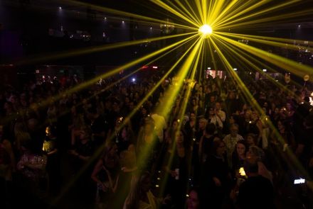 Multidão em casa de show, ambiente iluminado com jogo de luzes amarelas.