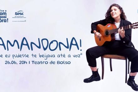 Artista Amandona. Mulher com cabelo cacheado está sentada em um banco, tocando violão e sorrindo.