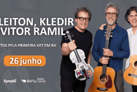 O anúncio apresenta um fundo cinza com marcas d'água das silhuetas dos próprios artistas. À direita, os três músicos aparecem sorridentes, em pé e lado a lado, segurando seus respectivos instrumentos acústicos: um violino decorado com desenhos coloridos, um violão e um violão de náilon menor. À esquerda, o texto em letras garrafais brancas destaca o nome do trio e a frase "JUNTOS PELA PRIMEIRA VEZ EM BH". Logo abaixo, a data "26 junho" ganha destaque dentro de um botão oval laranja, com os logotipos da Symp