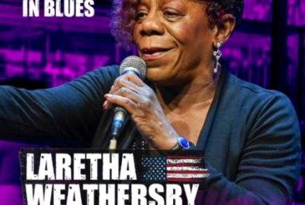 O cartaz do show Rota do Blues apresenta uma identidade visual marcante dominada por uma forte iluminação em tons de roxo e neon ao fundo. No centro da peça publicitária, destaca-se a fotografia em plano médio da cantora Laretha Weathersby, que aparece sorrindo de forma expressiva enquanto segura um microfone com a mão direita próximo ao rosto. Ela veste um casaco escuro sobre uma blusa preta, usa brincos compridos prateados em formato de clave de sol e uma boina preta brilhante com detalhes em strass na ab