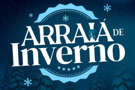 Este cartaz vertical anuncia o evento "Arraiá de Inverno" utilizando uma temática que mistura elementos juninos tradicionais com uma atmosfera gelada. O fundo exibe uma noite fria e estrelada sob o brilho de uma lua cheia isolada no canto superior direito. No centro, o título se destaca em letras brancas imponentes, parcialmente sobreposto a um grande selo circular azul-claro que é decorado com pequenas estrelas e flocos de neve flutuantes. A base da imagem contrasta o cenário frio de uma floresta de pinhei