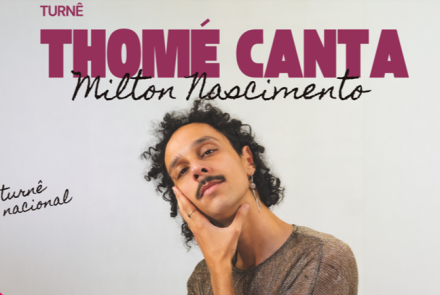 Cartaz de divulgação musical sobre fundo esbranquiçado. No centro, há a foto em meio-corpo de um cantor jovem de pele parda, cabelos pretos cacheados e bigode. Ele está com a cabeça levemente inclinada, apoiando o rosto com a mão direita, e usa uma blusa em tom metalizado ou dourado escuro.