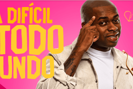 Imagem promocional com fundo rosa vibrante onde se destaca, à esquerda, o texto "TÁ DIFÍCIL PRA TODO MUNDO" escrito em letras amarelas e brancas. No centro, um homem negro sorri apontando o dedo indicador para a própria cabeça. Ele está cercado por dois pequenos cupidos negros de asas brancas e fralda segurando arco e flecha, além de um desenho de coração partido na parte superior.