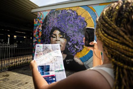 Garota tirando foto de mural, segurando o mapa da região central de BH