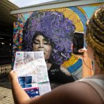 Garota tirando foto de mural, segurando o mapa da região central de BH
